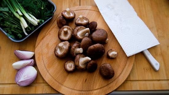 Wooden cutting board with mushrooms, green onions, and a knife on a wooden surface