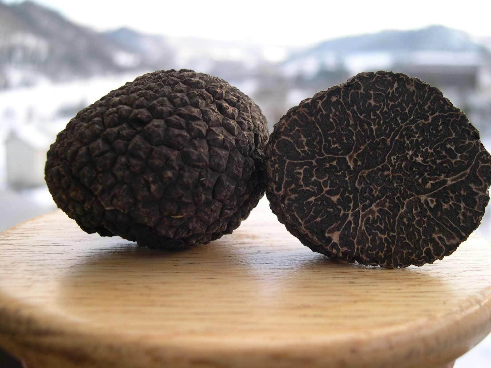 Two black truffles on a wooden surface with a blurred background
