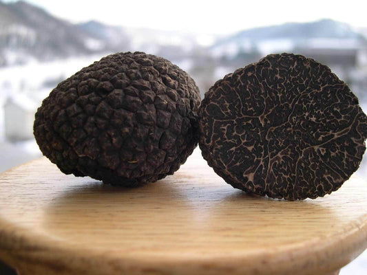 Two black truffles on a wooden surface with a blurred background